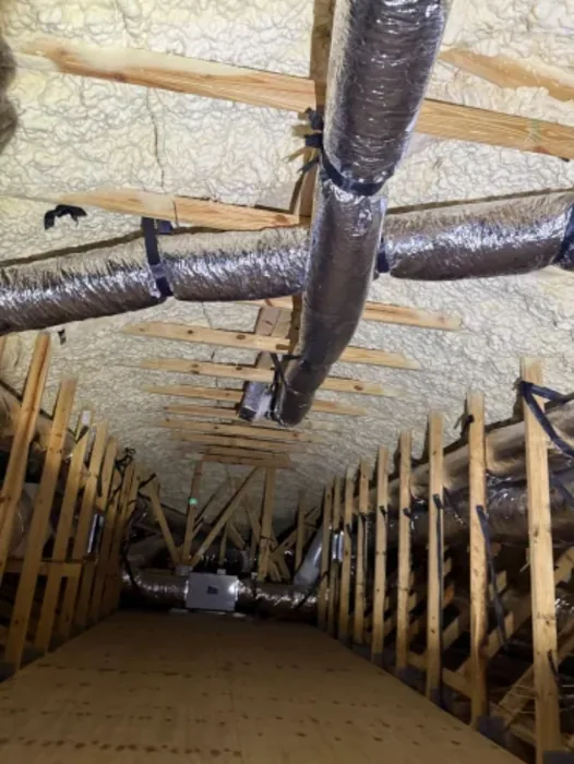 Flexible ductwork running through a Florida attic with spray foam insulation and wood trusses