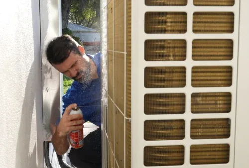 Cleaning an outdoor AC condenser coil with a hose during maintenance service in Belleair, Florida
